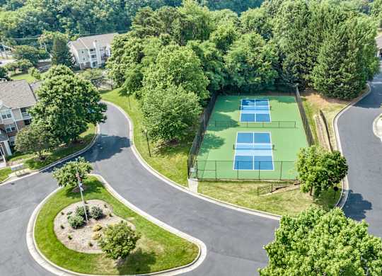 A tennis court is surrounded by trees and a road. at Sunscape Apartments, Roanoke, Virginia