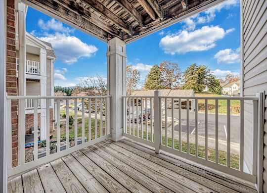 A balcony with a white railing and wooden floor overlooks a parking lot. at Sunscape Apartments, Roanoke