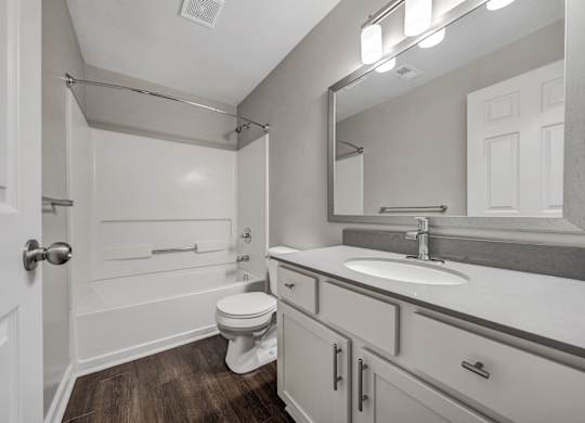 A white bathroom with a toilet, sink, and mirror. at Sunscape Apartments, Roanoke, 24018