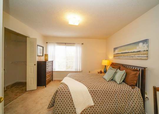 A bedroom with a bed, dresser, and a walk-in closet at Tall Oaks Apartment Homes, Michigan