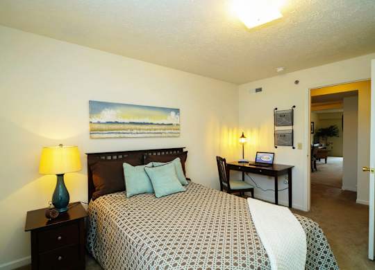 A bedroom with a bed, desk, and plush carpeting at Tall Oaks Apartment Homes, Michigan