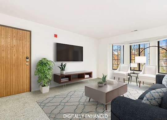 A living room with bay windows, a grey couch, a television, and a rug at Tanglewood Apartments, Oak Creek