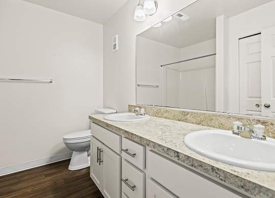 A bathroom with a toilet, two sinks, and mirror at Tanglewood Apartments, Oak Creek, WI