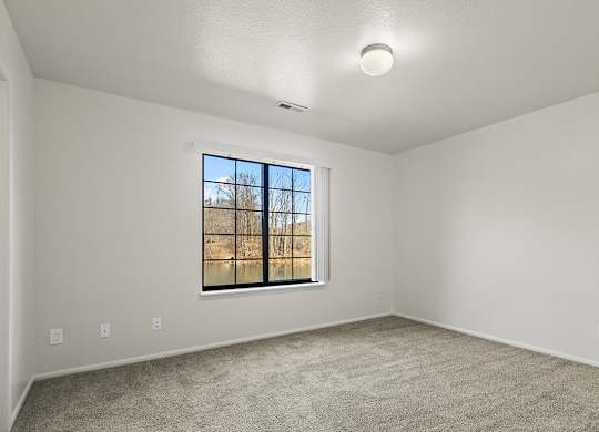 A spacious bedroom with a window and a carpeted floor at Tanglewood Apartments, Oak Creek, WI