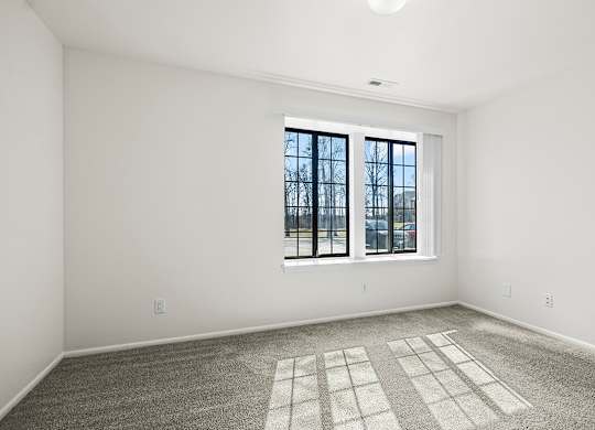 A spacious bedroom with a large window and a carpeted floor at Tanglewood Apartments, Oak Creek, WI