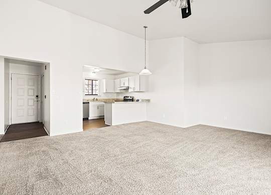 A large, empty dining and living room with a carpeted floor and a kitchen area in the background at Tanglewood Apartments, Oak Creek, WI