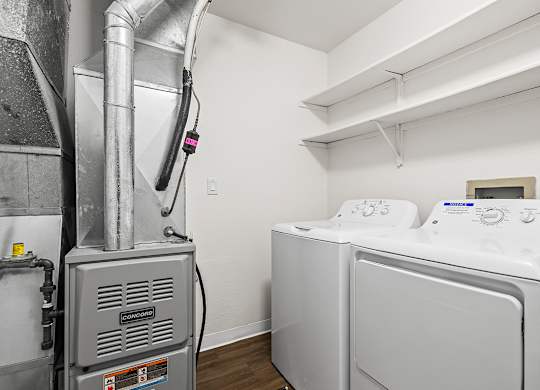 A washing machine is in a laundry room with a dryer and shelves at Tanglewood Apartments, Oak Creek, WI