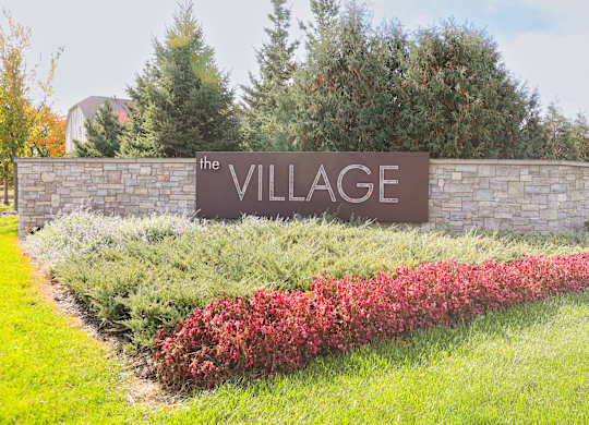 a sign for the village on a stone wall with flowers