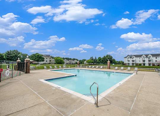 A large swimming pool surrounded by a concrete patio and lounge chairs at The Crossings Apartments, Michigan