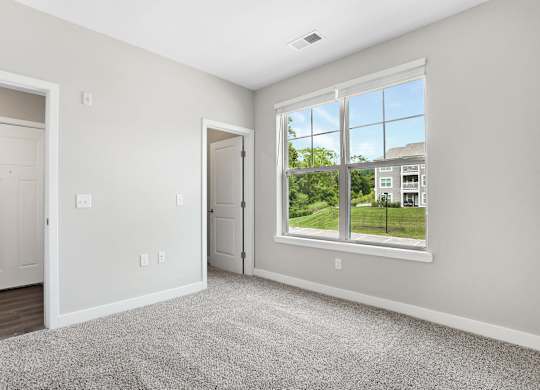 A room with a carpeted floor, two doors, and a window showing an outdoor view at The Retreat Apartments, Roanoke, 24019