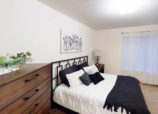 A bedroom with a bed, nightstand, and a potted plant at Tracy Creek Apartment Homes in Perrysburg, OH