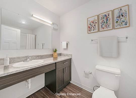 A main bathroom with a toilet, sink, mirror, and pictures on the wall at Trade Winds Apartment Homes, Elkhorn, Nebraska