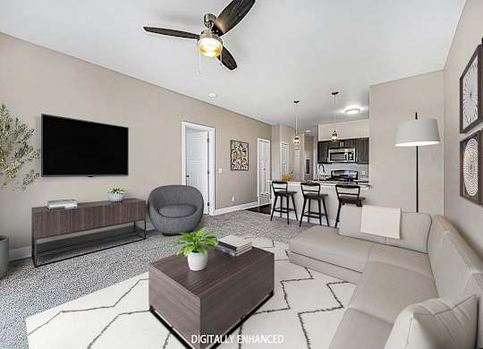 A living room with a grey armchair, a white sofa, a wooden coffee table, and a ceiling fan at Trade Winds Apartment Homes, Elkhorn, Nebraska