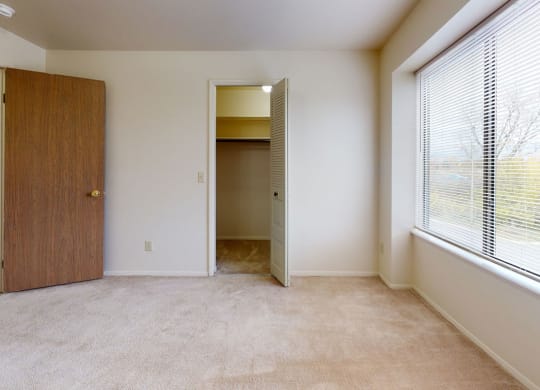 a bedroom with a large window and a door to a closet  at Trappers Cove Apartments, Michigan