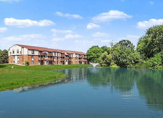 A large building with a red roof is situated next to a body of water at Trappers Cove Apartments, Lansing, 48910