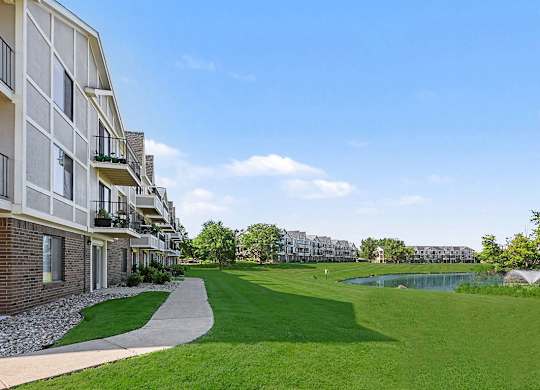 A sunny day at a residential complex with a grassy area and a pond at Trappers Cove Apartments, Lansing, 48910