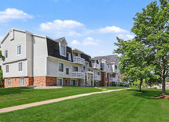 An apartment building with green lawn and sidewalk at Trappers Cove Apartments, Lansing, 48910