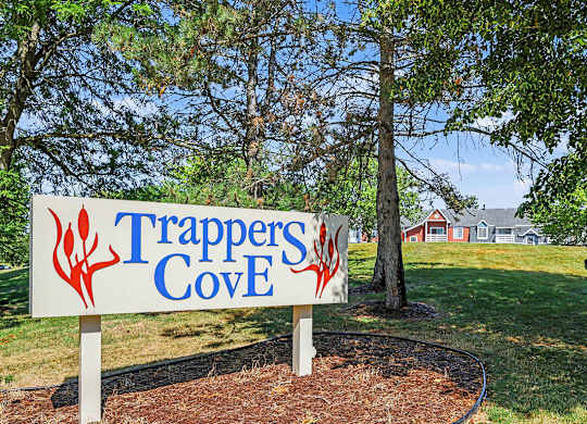 A sign that says Trappers Cove is in front of a tree at Trappers Cove Apartments, Lansing, MI, 48910