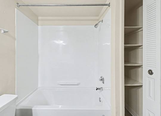 A white bathroom with a tub, shower and a linen closet at Trappers Cove Apartments, Lansing