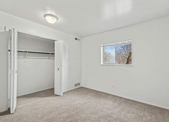 A white bedroom with a window and a white closet at Trappers Cove Apartments, Lansing