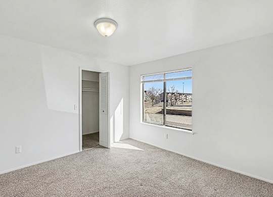 A bedroom with a carpeted floor, a large window, and a closet at Trappers Cove Apartments, Lansing