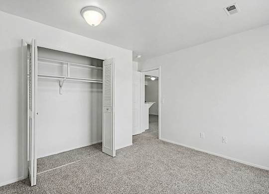 A white bedroom with a large closet and carpet at Trappers Cove Apartments, Lansing