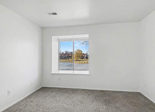 A bedroom with a large window showing a view of a pond at Trappers Cove Apartments, Lansing