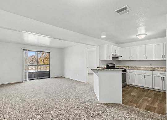A spacious living room and an upgraded kitchen with white cabinets and a slider to a balcony at Trappers Cove Apartments, Lansing