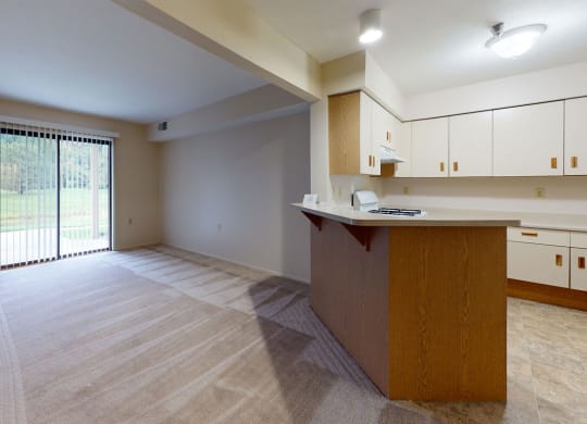 an empty living room and kitchen with a sliding glass door at Trillium Pointe Apartment Homes, Jackson, MI