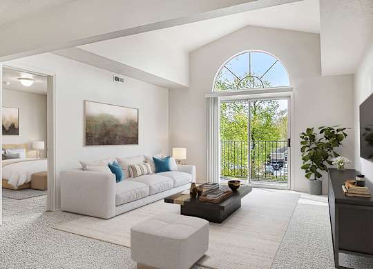 A living room with a cathedral ceiling, large window and sliding glass doors to a balcony at Trillium Pointe Apartment Homes, Jackson, MI