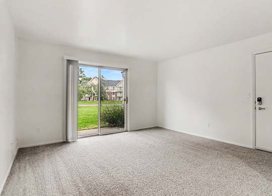 A living room with a carpeted floor and a sliding glass door leading to a patio and green lawn at Walnut Trail Apartments, Michigan