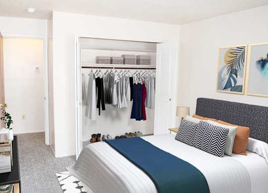 A bedroom with a large bed and a closet with clothes hanging at Walnut Trail Apartments, Portage, MI, 49002