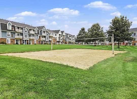 A volleyball net is set up on a sandy court in front of apartment buildings at Walnut Trail Apartments, Michigan