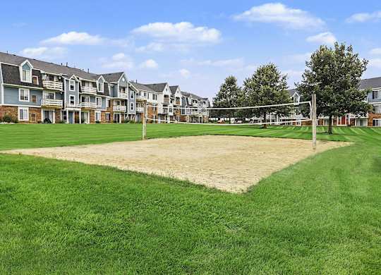 A volleyball net is set up on a sandy patch in the middle of a grassy area at Walnut Trail Apartments, Portage, MI