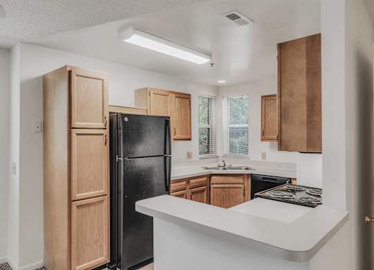 A kitchen with a black refrigerator and wooden cabinets at WaterFront Apartments, Virginia Beach, 23453