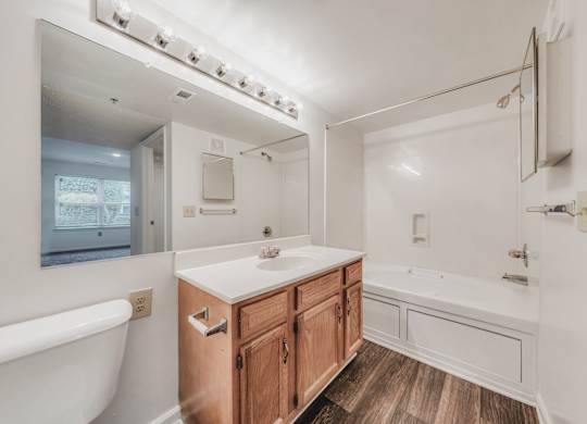 A white bathroom with a wooden vanity and a white bathtub at WaterFront Apartments, Virginia Beach, 23453