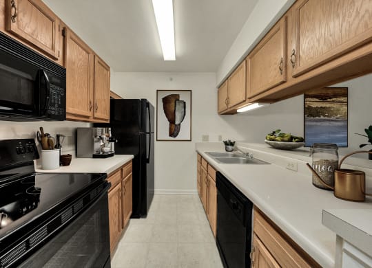 a kitchen with wood cabinets and black appliances and white counter tops at WaterFront Apartments, Virginia Beach, VA