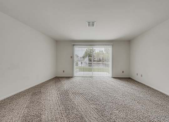 A room with a carpeted floor and a view of a fence and trees outside through a sliding glass door at WaterFront Apartments, Virginia Beach, 23453