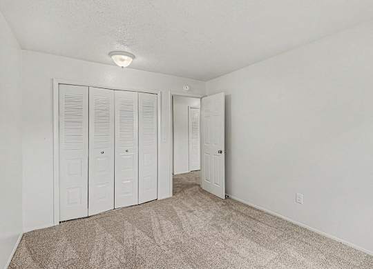 A bedroom with white walls and a carpeted floor with a large white closet at Waverly Park Apartments, Lansing