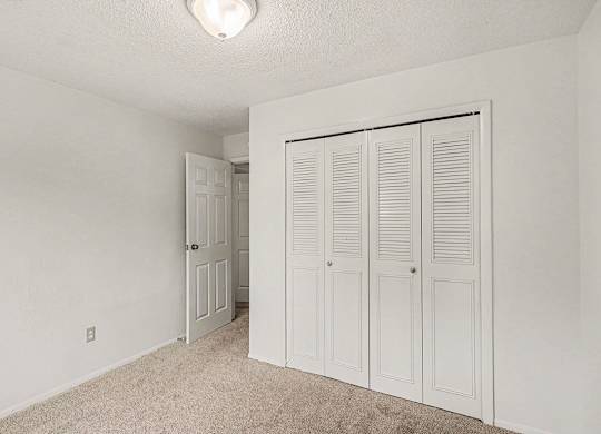 A white bedroom with a carpeted floor and a white door to a closet at Waverly Park Apartments, Lansing