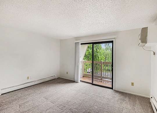 A living room with a carpeted floor and a sliding glass door leading to a balcony at Waverly Park Apartments, Lansing