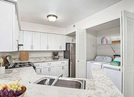 A kitchen with a breakfast bar, white cabinets and a washer/dryer at West Hampton Park Apartments in Elkhorn, NE 68022