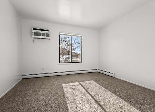 A spacious bedroom with a carpet, a window, and an air conditioner at Wood Creek Apartments, Kenosha