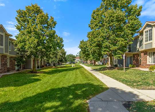 A green, well manicured lawn and trees outside apartment buildings at Wood Creek Apartments in Kenosha, WI