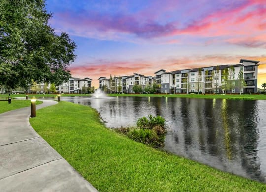 a sidewalk next to a lake with a fountain at Pearce at Pavilion Luxury Apartments, Riverview, Florida