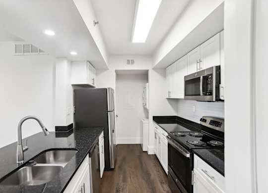 A modern kitchen with stainless steel appliances, black countertops and white cabinets.