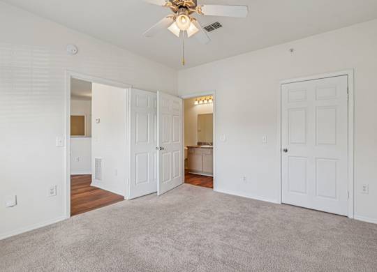 A spacious bedroom with a ceiling fan, carpeted floor and attached bathroom
