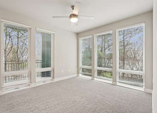 A large bedroom with floor to ceiling windows all through out the room,  a ceiling fan