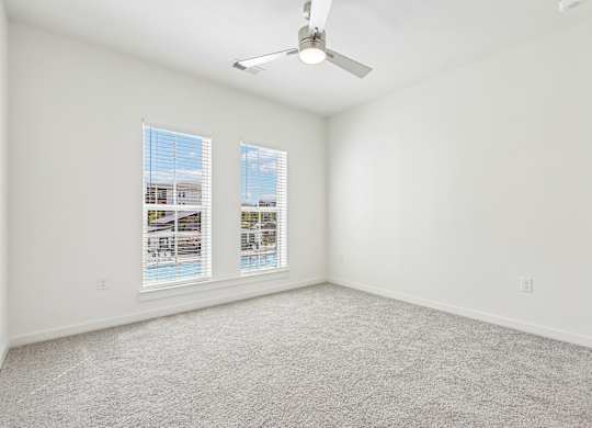 A room with a carpet floor, a ceiling fan, and two windows.