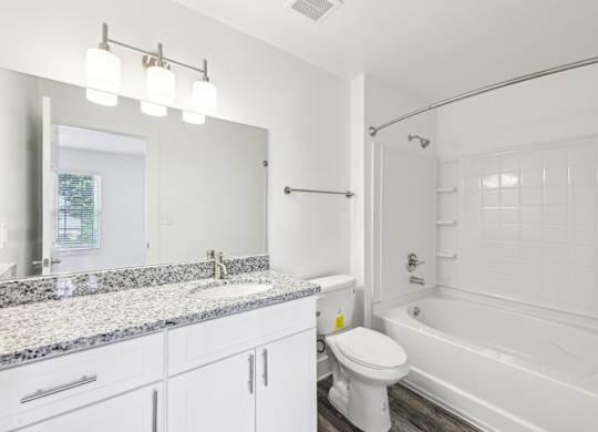A white bathroom with a granite countertop and a white toilet.